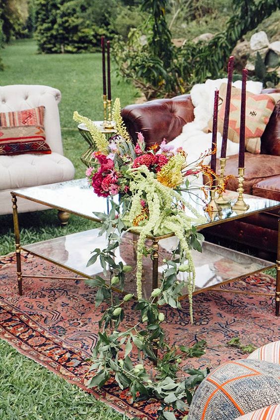 a bold boho wedding lounge with a leather sofa, a white chair, printed pillows, purple candles, bold blooms and greenery