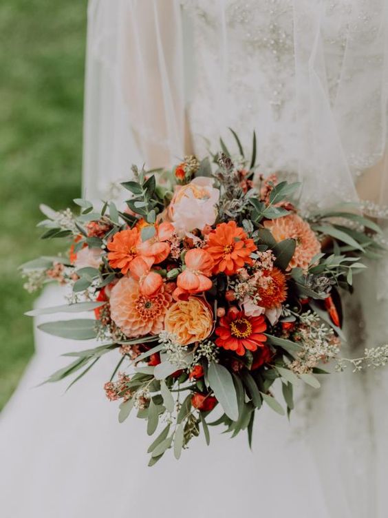 a bold orange wedding bouquet with touches of blush and red blooms, lots of greenery and some berrries will fit a summer or fall wedding