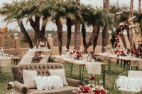 a bold outdoor wedding lounge with a grey loveseat, metal chairs, poufs and pillows, a rug, a low coffee table and bold blooms