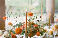 a bold textural and dimensional wedding centerpiece with neutral and orange blooms and greenery and orange candles