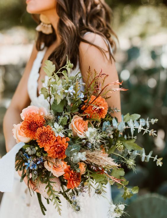 a bold textural wedding bouquet of orange and peachy blooms, lots of textural greenery and blue flowers is wow