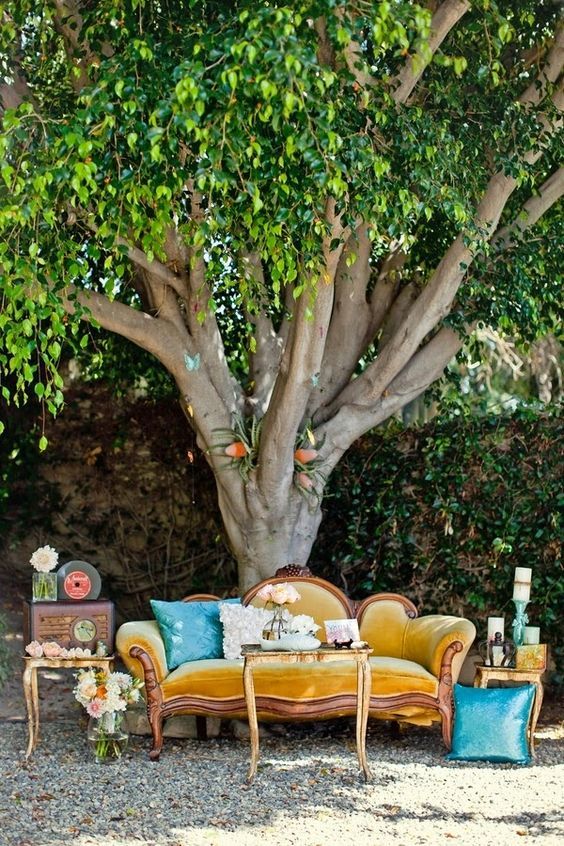 a bold vintage outdoor wedding lounge with a mustard sofa, blue pillows, side tables with candles under a tree