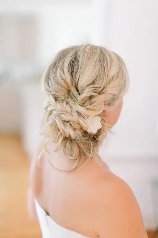 a braided messy low updo with a flower tucked inside and some little curls down is a cool idea if you want something wearable and still very romantic