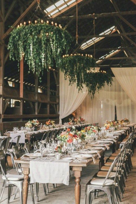 a bright and cool barn wedding reception with greenery chandeliers with candles, bright blooms and greenery and neutral linens