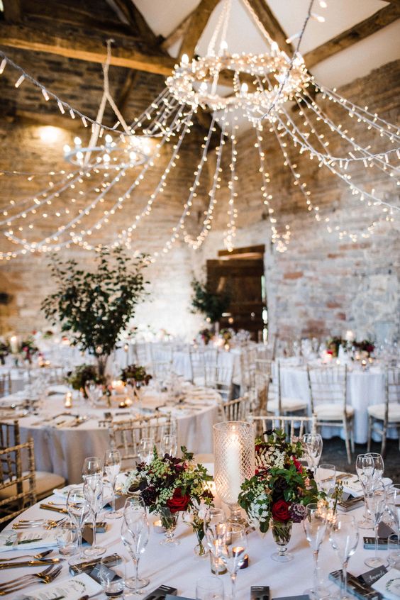 a bright barn wedding reception with lights, greenery and bold blooms plus candles on the table