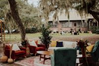 a bright boho outdoor wedding lounge with red and green chairs, a neutral sofa and bright pillows, a coffee table and layered rugs