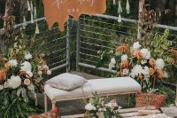 a bright boho wedding lounge with bold and lush blooms, a pallet coffee table, a printed rug and pillows, a bench and tassels