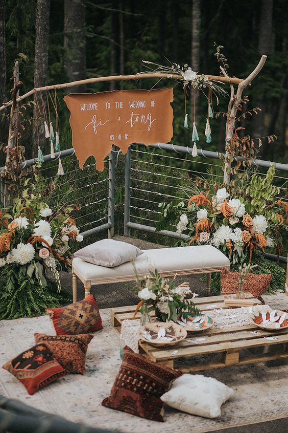a bright boho wedding lounge with bold and lush blooms, a pallet coffee table, a printed rug and pillows, a bench and tassels