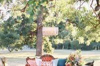 a bright outdoor wedding lounge with refined furniture – an orange sofa, green chairs, a coffee table and bold blooms and a crystal chandelier