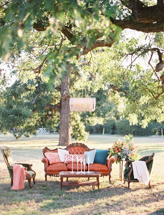 a bright outdoor wedding lounge with refined furniture - an orange sofa, green chairs, a coffee table and bold blooms and a crystal chandelier
