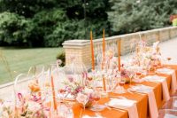 a bright wedding tablescape with an orange tablecloth and candles, blush and pink florals and elegant blush textiles