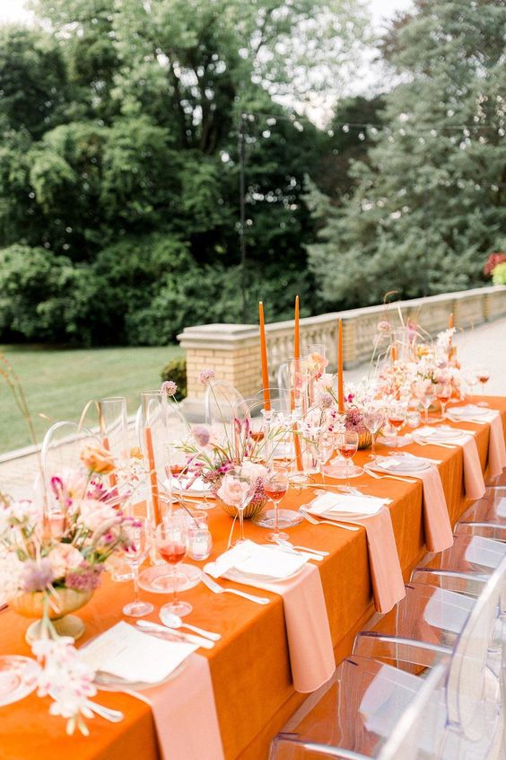 a bright wedding tablescape with an orange tablecloth and candles, blush and pink florals and elegant blush textiles