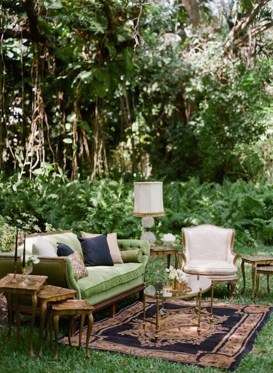 a chic vintage outdoor wedding lounge with a green sofa and neutral chairs, a range of vintage coffee tables and a printed rug