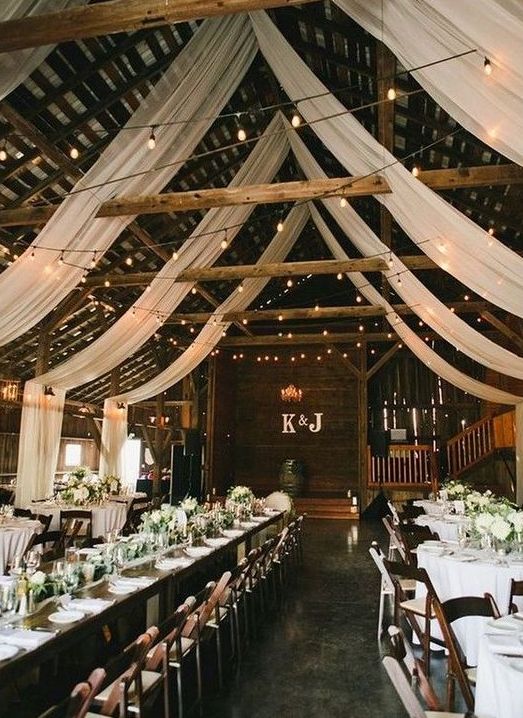 a chic wedding reception space with white fabric, lights, neutral blooms and greenery is a very welcoming space