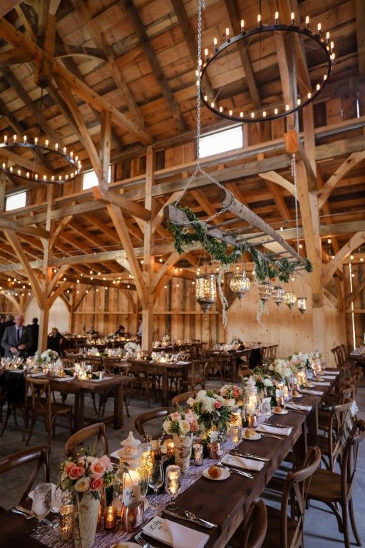 a cool barn wedding reception with chandeliers, a greenery hanging with candles and sticks and bright blooms