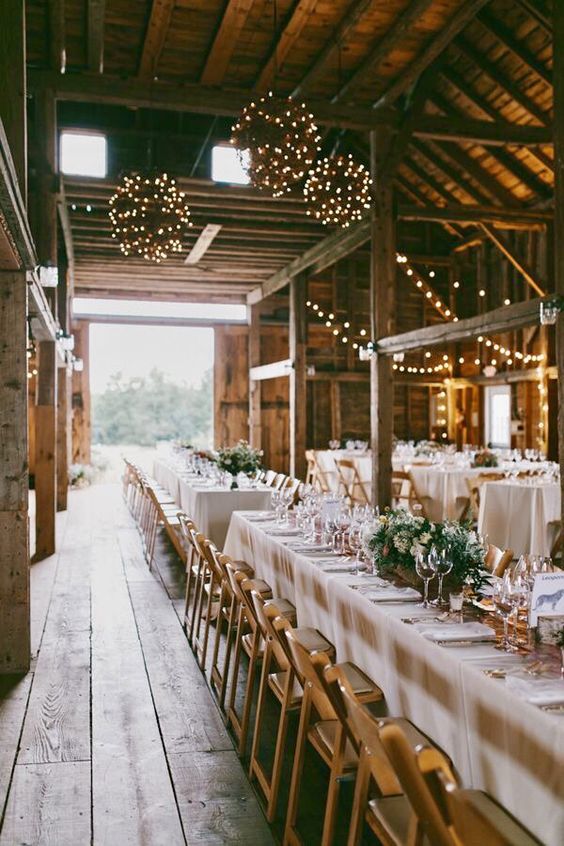 a cool barn wedding reception with greenery and neutral blooms, candles, lights and light spheres