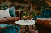 a dark and moody boho wedding lounge with teal vintage chairs, leather sofas with blue pillows, a printed rug and a round table