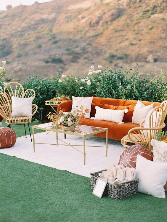 a fab boho wedding lounge with an orange sofa, rattan chairs, a glass coffee table, neutral pillows and leather poufs