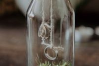 a glass bottle filled with moss and with rings attached to the cork is a cool woodland wedding idea