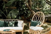 a gorgeous tropical wedding lounge with rattan furniture, neutral and green pillows, a round table and a neutral rug