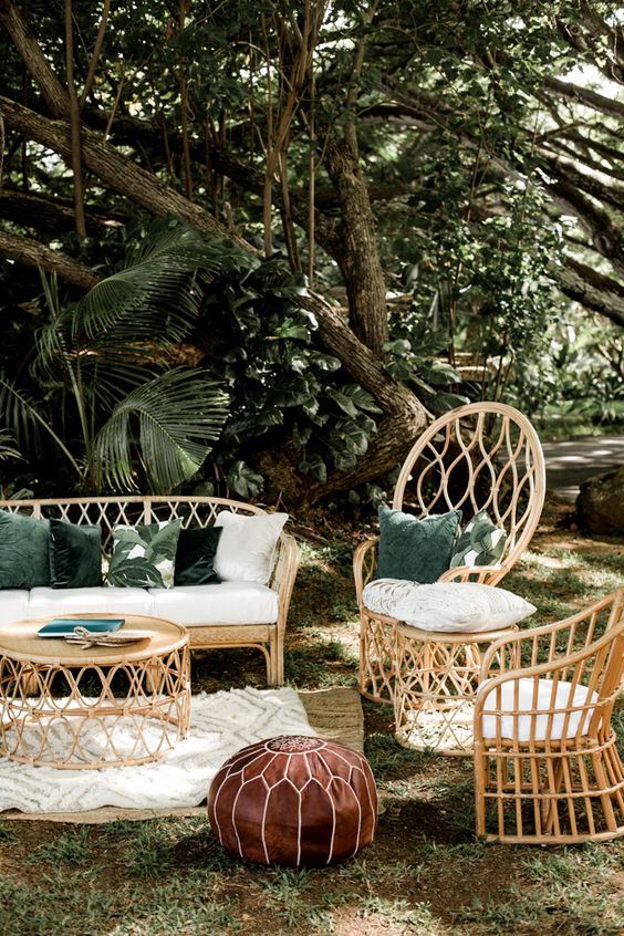 a gorgeous tropical wedding lounge with rattan furniture, neutral and green pillows, a round table and a neutral rug