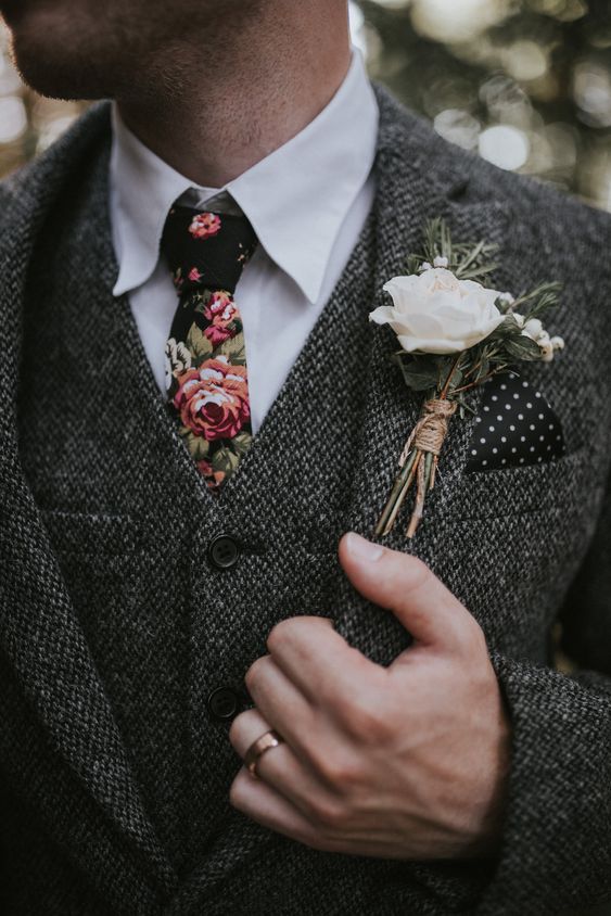 a grey tweed three-piece suit, a white button down and a moody floral tie plus a floral boutonniere