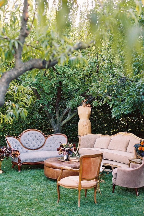a hidden garden wedding lounge with elegant pastel furniture, a leather ottoman, a vintage chair and dark blooms