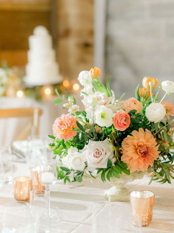 a lovely neutral wedding tablescape with orange and white blooms and greenery, candles is a lovely idea for a summer wedding