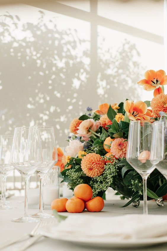 a lush and bold wedding centerpiece of greenery and orange blooms plus some tangerines for summer