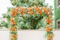 a lush wedding arch covered with lots of greenery and bold orange blooms is a fantastic idea for a summer wedding