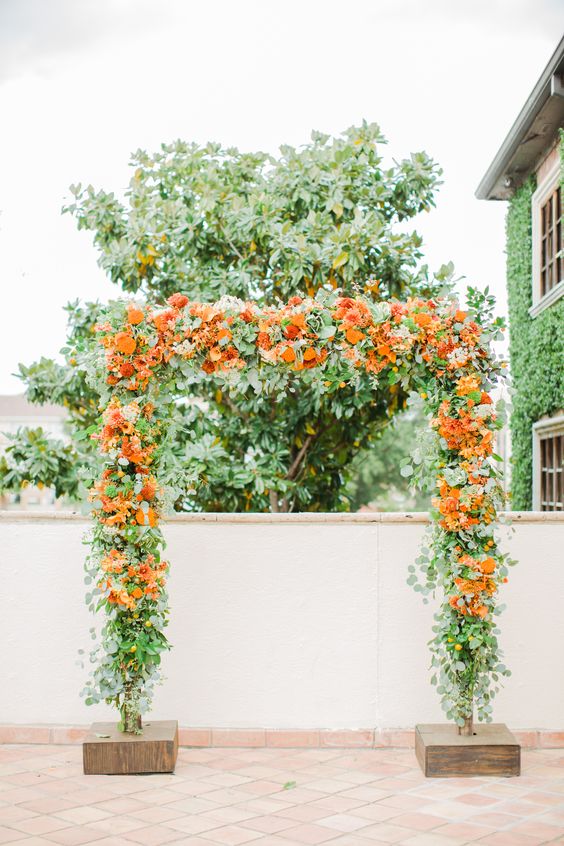 a lush wedding arch covered with lots of greenery and bold orange blooms is a fantastic idea for a summer wedding