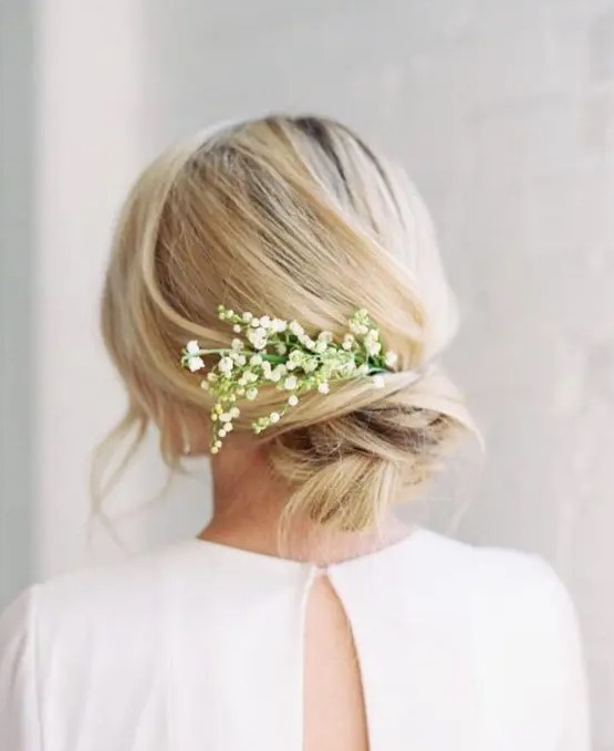 a messy twisted chignon with some bangs and lily of the valley tucked in is a romantic idea for a spring bride, at a beach or some other wedding