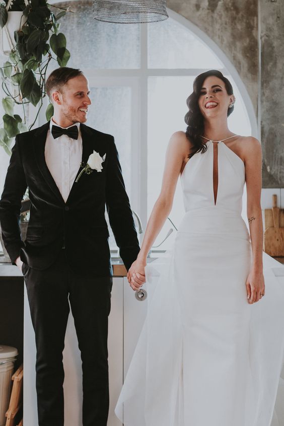 a minimalist sheath wedding dress with a halter neckline, a deep cut on the front and a tulle skirt behind