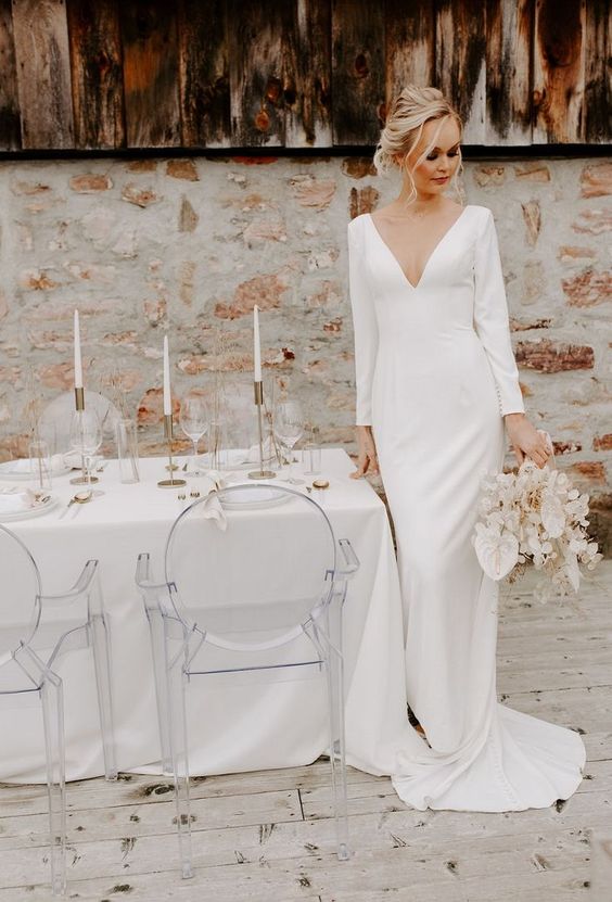 a minimalist sheath wedding dress with a plunging neckline, long sleeves, a train for a refined modern bride