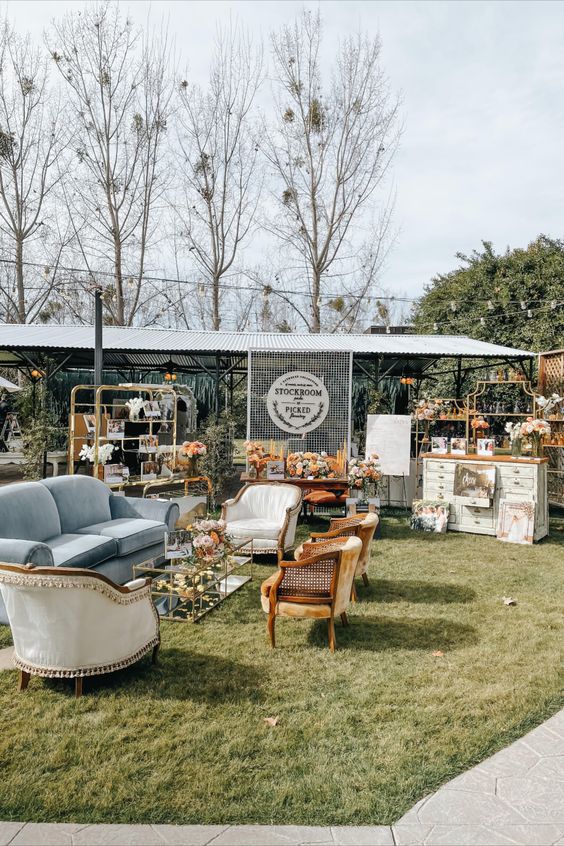 a modern boho wedding lounge with a dusty blue sofa, neutral chairs, a glass coffee table with blooms and a bar on its side