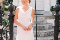 a modern white midi dress with a cowl neckline, no sleeves and an asymmetric skirt plus statement earrings