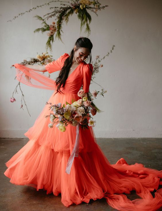 a neon orange A-line wedding dress with a depe neckline, puff sleeves, a long train is amazing for summer or fall