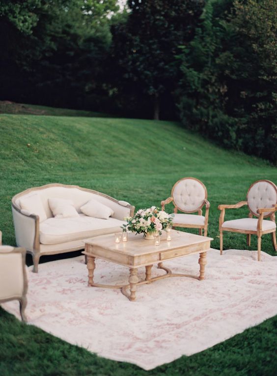 a neutral vintage wedding lounge with refined and chic furniture, a printed rug, a low coffee table and some neutral blooms