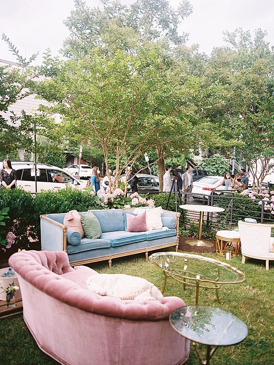 a pastel outdoor wedding lounge with a pink and blue sofa, pastel pillows, glass coffee tables and candleholders