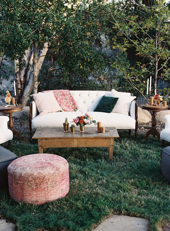 a pretty boho wedding lounge with white seating furniture, white and green pillows, chic coffee tables and a pink pouf