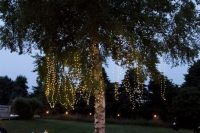 a relaxed and cool outdoor wedding lounge with rugs and pillows on the grass, candle lanterns and lights hanging on the tree