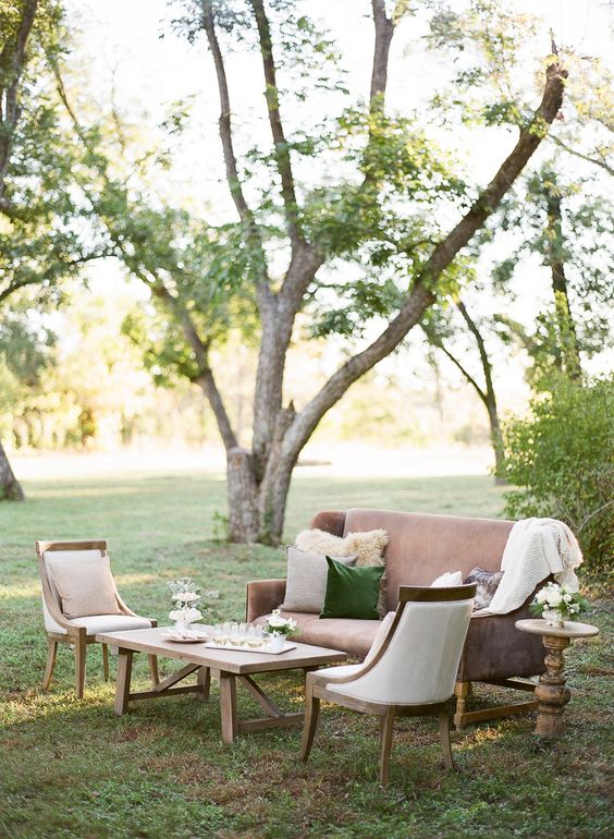 a relaxed neutral outdoor wedding lounge with a mauve sofa and white chairs, a wooden coffee table and white blooms