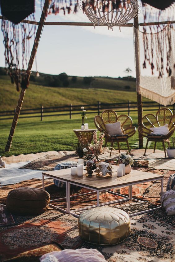 a relaxed outdoor boho wedding lounge with a low coffee table, lots of layered rugs, poufs and pillows, rattan chairs and tassels