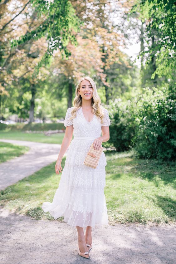 a romantic A-line midi dress with a tiered skirt with ruffles, short sleeves and a cutout neckline, nude heels and a wicker clutch
