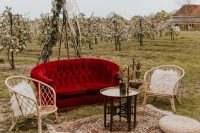 a simple boho outdoor wedding lounge with a bold red foa and rattan chairs, jute poufs, a printed rug and a coffee table