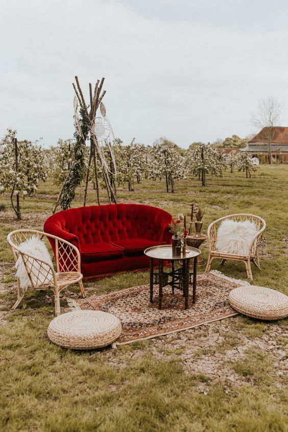 a simple boho outdoor wedding lounge with a bold red foa and rattan chairs, jute poufs, a printed rug and a coffee table