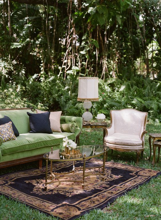 a sophisticated garden wedding lounge with a green sofa, a neutral chair, a glass coffee table, a printed rug and some bold pillows