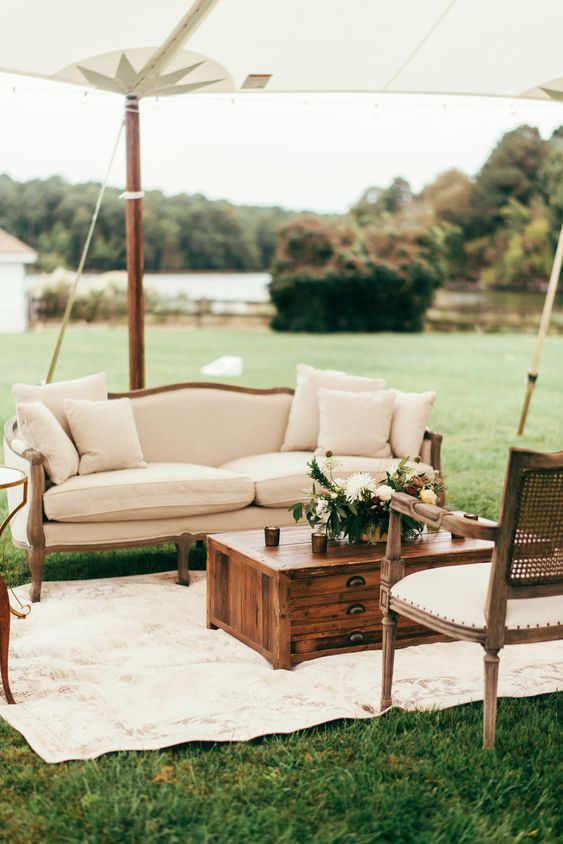 a stylish neutral vintage wedding lounge with a sofa, some chairs, a stained chest for storage and some neutral blooms