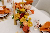 a super bold wedding tablescape with rust napkins, with yellow, red and orange blooms and gold cutlery
