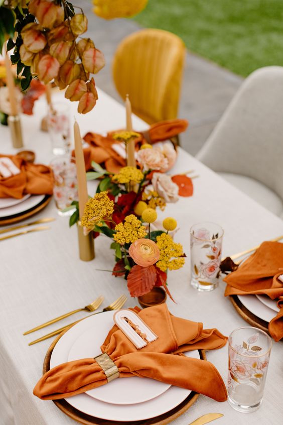 a super bold wedding tablescape with rust napkins, with yellow, red and orange blooms and gold cutlery